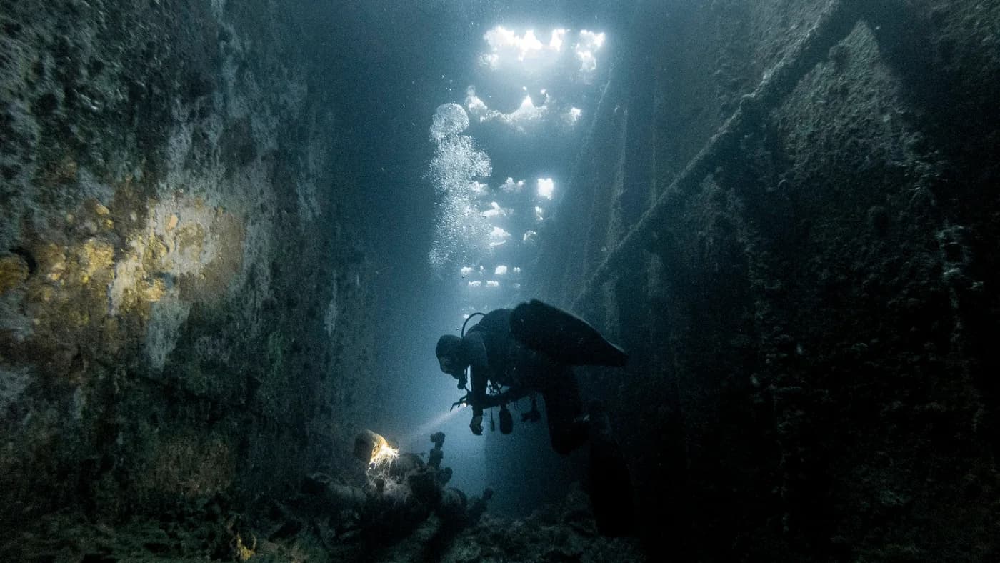 Un plongeur explore une épave éclairée par la lumière de la surface, dans le lagon de Chuuk