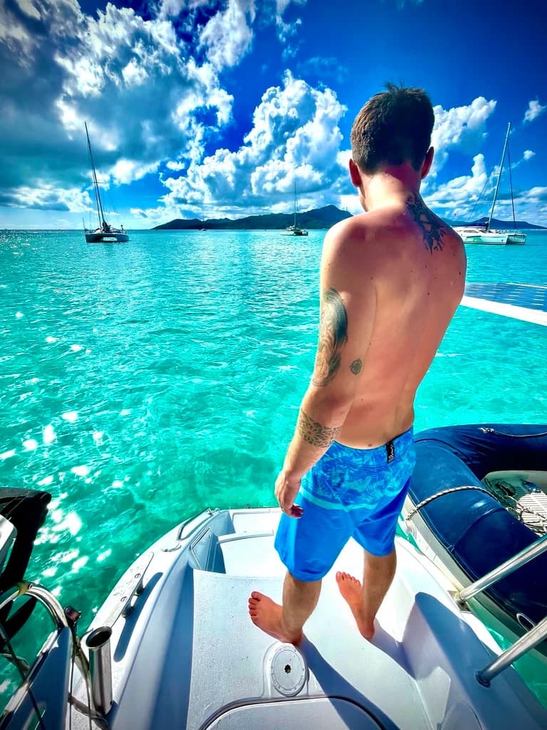 Nicolas Idelot, de dos sur un bateau, face à une mer turquoise et à des voiliers